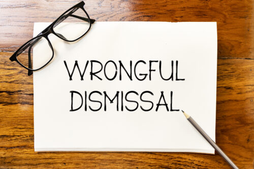 Wrongful dismissal text on blank notebook paper on wooden table with pencil and glasses aside. Business concept and legal concept about wrongful dismissal.